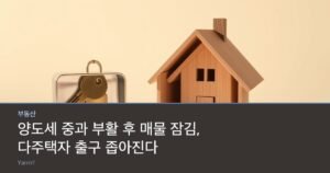 A brass door key inside a small padlocked metal box beside a miniature wooden house model on a bright table