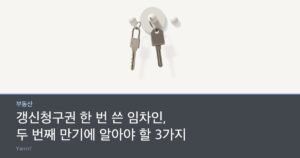 Two identical door keys hanging on a bright wall hook above a rolled paper document tied with string